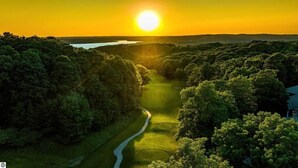 Ein Golfplatz mit einem gewundenen Weg, umgeben von dichten Bäumen und einem Sonnenuntergang im Hintergrund.