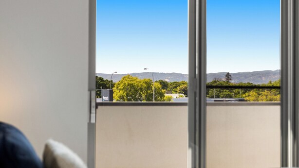 Een slaapkamer met een bed, kussens en een groot raam met uitzicht op een balkon en verre bergen.