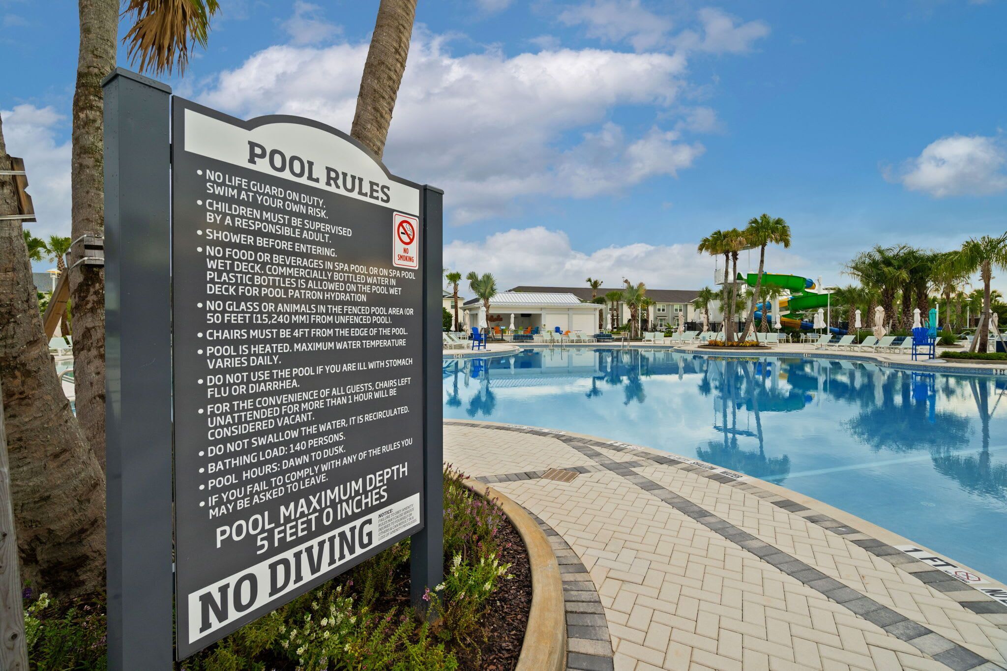 A pool with clear water, surrounded by palm trees and a sign listing pool rules.