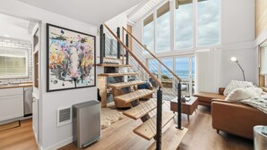 Una sala de estar moderna con una escalera de madera, un ventanal grande y un cuadro en la pared.