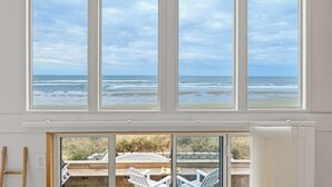 Una habitación con grandes ventanales que dan al océano, una terraza de madera con sillas y vistas a la playa.