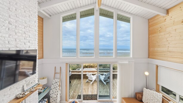 Una habitación amplia con un gran ventanal con vista al mar, ventilador de techo y un rincón de descanso acogedor con vistas.