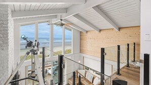 A modern interior with a wooden ceiling, large windows overlooking a beach, and a telescope on a tripod. - NEW Beachfront Escape, Hot Tub, Ocean Views, Dunes (Rockaway Beach)
