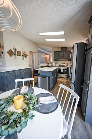 A modern kitchen with grey cabinets, a central island, and a dining area with a white table and chairs.