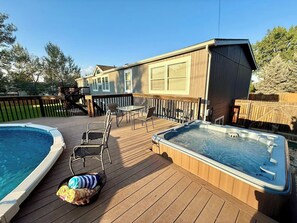 Un jardin avec une piscine, un jacuzzi, des chaises longues et une clôture en bois.