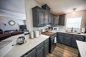 A modern kitchen with dark cabinetry, a central island, a microwave, and a stove.