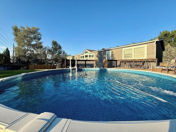 A rectangular swimming pool with a wooden deck and lounge chairs.