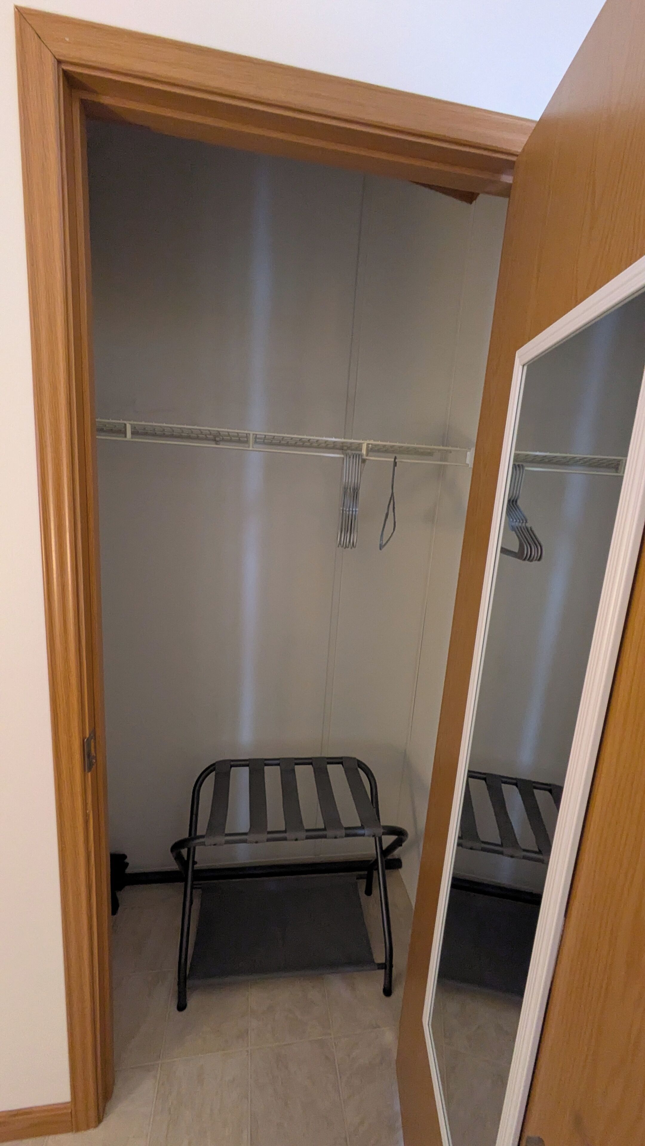 Une pièce avec une porte en bois, un banc en métal et une porte de placard en miroir.