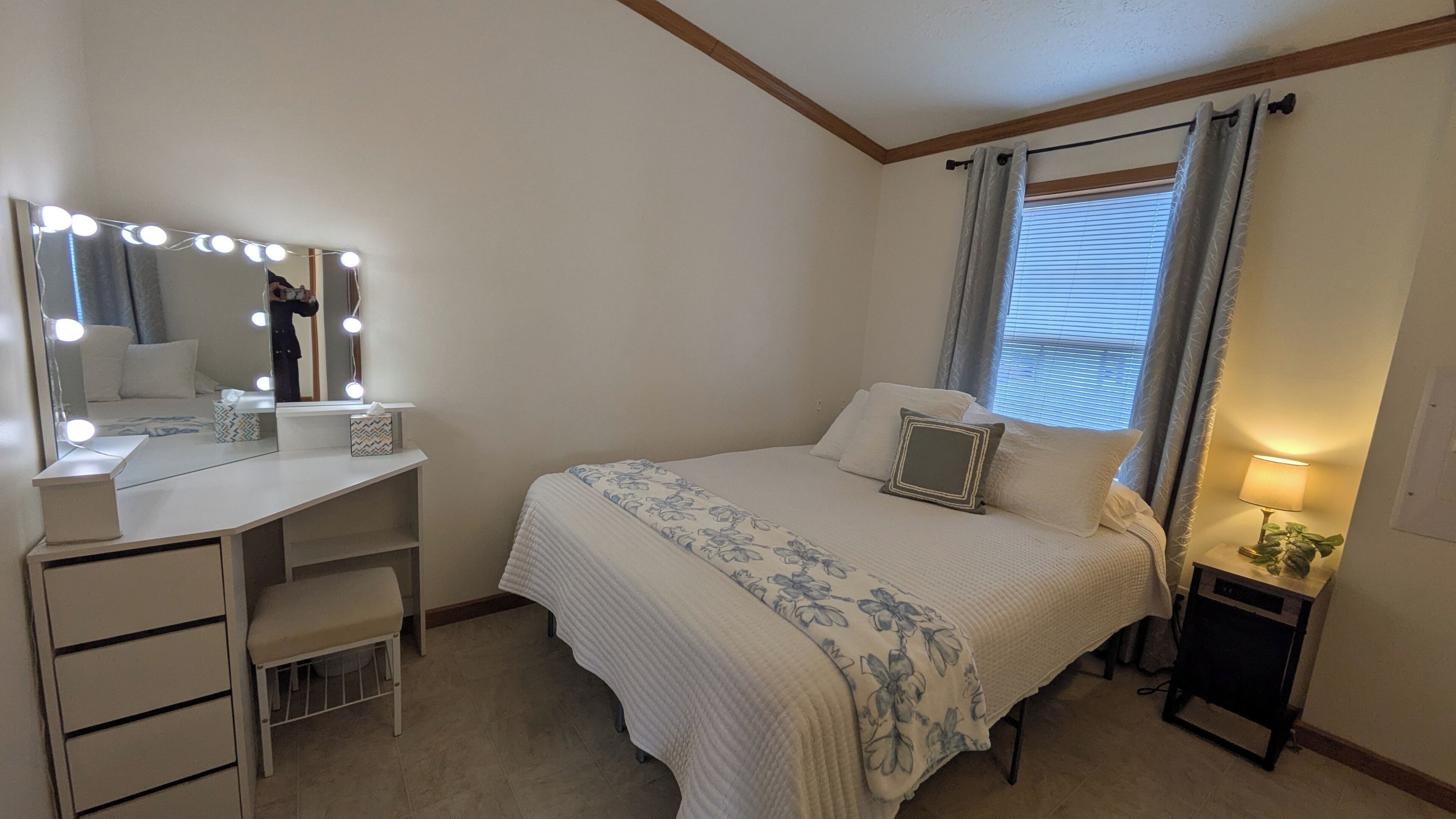 Une chambre à coucher comprenant une coiffeuse, un lit et une table de chevet avec une lampe.
