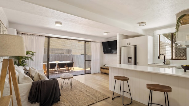 Une cuisine moderne dotée d’un grand îlot central, de tabourets de bar et d’une porte-fenêtre coulissante donnant sur un patio.