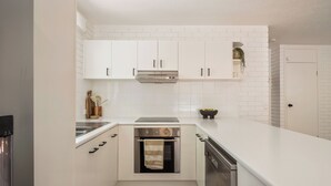 Une cuisine de taille réduite avec des meubles blancs, un four en acier inoxydable et un lave-vaisselle.