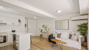 Une cuisine moderne avec des meubles blancs, un îlot central et un coin repas comprenant un canapé blanc et une table basse.