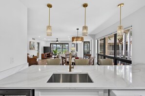 Une cuisine moderne dotée d’un grand îlot central, d’un évier en acier inoxydable et de luminaires suspendus.