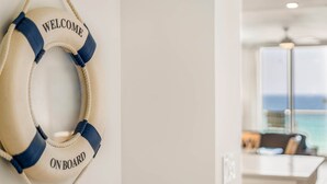 En livboj med texten ”VÄLKOMMEN OM BORD”, ett köksområde och utsikt över havet genom stora fönster.