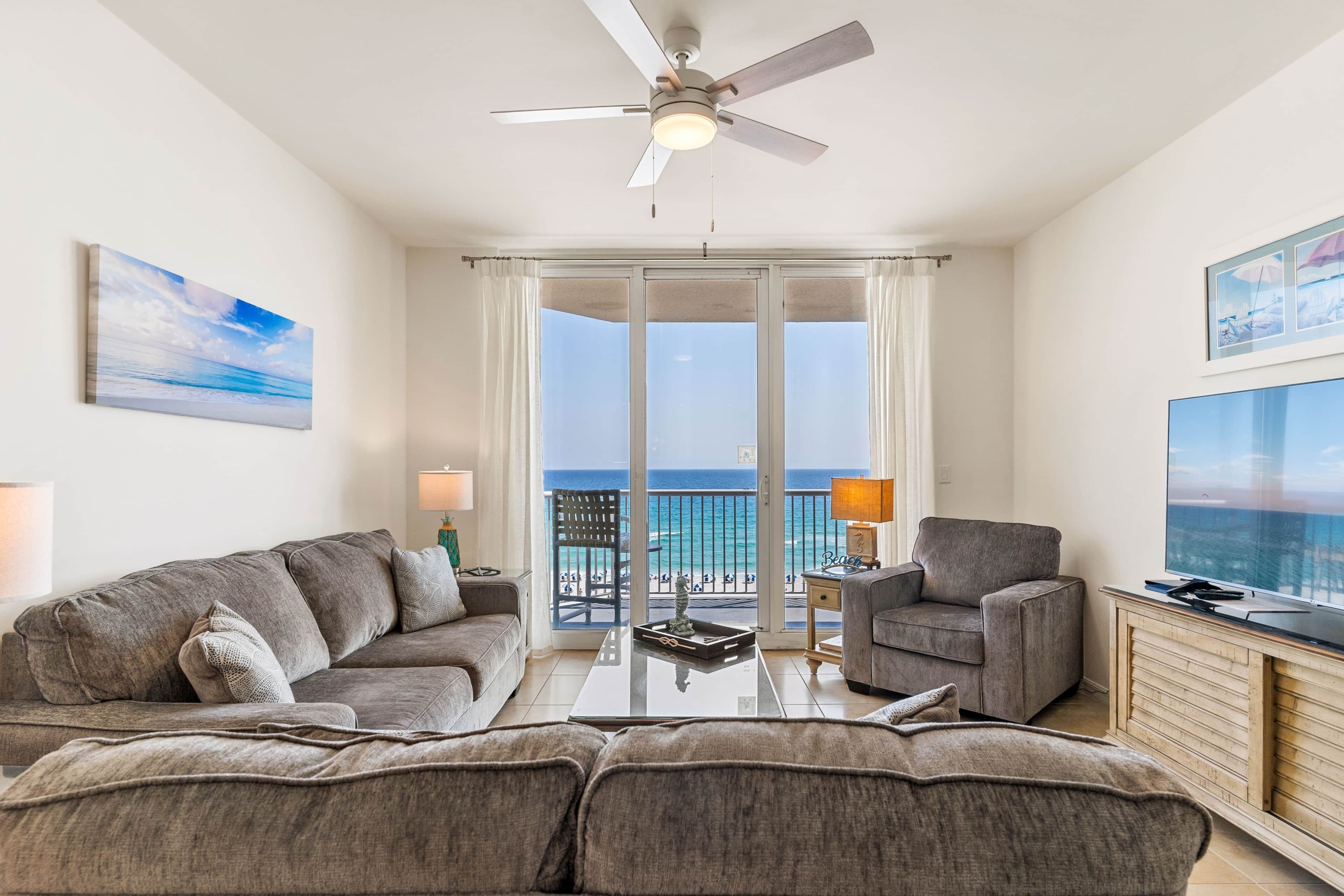 A modern living room with a ceiling fan, a sofa, a coffee table, and a view of the ocean through large windows.