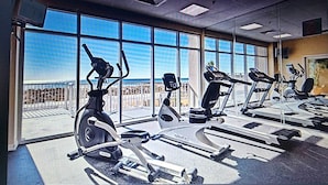 Ein Fitnessstudio mit verschiedenen Trainingsgeräten, großen Fenstern und Blick auf den Strand.