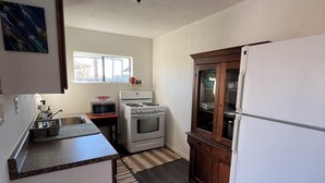 A compact kitchen with a built-in oven, a refrigerator, and a microwave. There is a window providing natural light and a small rug on the floor. - Cozy 1-bedroom bungalow in amazing Las Cruces with AC (Las Cruces)