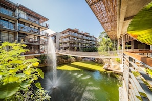 A modern building with multiple balconies, a central water feature, and a wooden bridge. - Tulum Premium Maisonette | Jacuzzi & Cenote (Tulum)