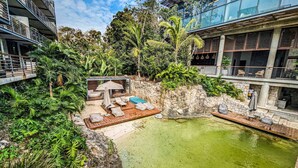 A rooftop pool area with lounge chairs and umbrellas, surrounded by lush greenery and modern buildings. - Nuju Rentals|Premium Apt| Jacuzzi,Cenote,Gym&Sauna (Tulum)
