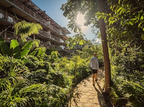 A person walking on a stone path surrounded by lush greenery and a multi-story building with balconies. - Tulum Premium Maisonette | Jacuzzi & Cenote (Tulum)
