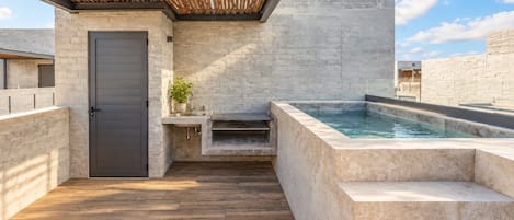 A modern outdoor bathroom with a stone wall, a wooden floor, a built-in sink, and a hot tub.
