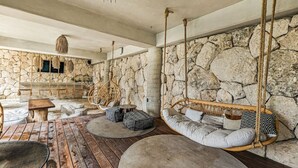 A rustic interior with stone walls, wooden flooring, and a hanging swing chair. - Nuju Rentals|Premium Apt| Jacuzzi,Cenote,Gym&Sauna (Tulum)