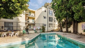 A swimming pool with a tiled edge, surrounded by a fence, and adjacent to a building with balconies and outdoor seating. - Cozy Private Suite • 10 Min to SoFi/Intuit/LAX/Manhattan & Venice Beach (Inglewood)