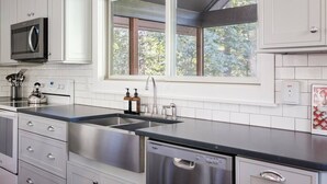 Une cuisine moderne avec des meubles blancs, un lave-vaisselle en acier inoxydable, un évier à deux bacs et un four à micro-ondes.
