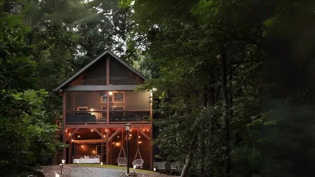 Une cabane en bois à deux étages, dotée d’un balcon et entourée d’une forêt dense.