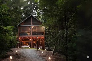 Une cabane en bois à deux étages, dotée d’un balcon et entourée d’une forêt dense.