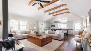 Un salon spacieux avec un plafond haut, des poutres apparentes, un grand canapé, une table basse et une cheminée.