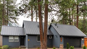 Une maison à deux étages, à l’extérieur de couleur gris foncé, avec un garage doté d’une porte en bois et une cour avant bien entretenue, agrémentée de petits arbustes.