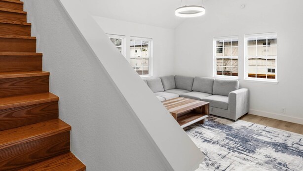 Un intérieur moderne avec un escalier en bois, un canapé d’angle gris, une table basse en bois et un tapis à motifs.