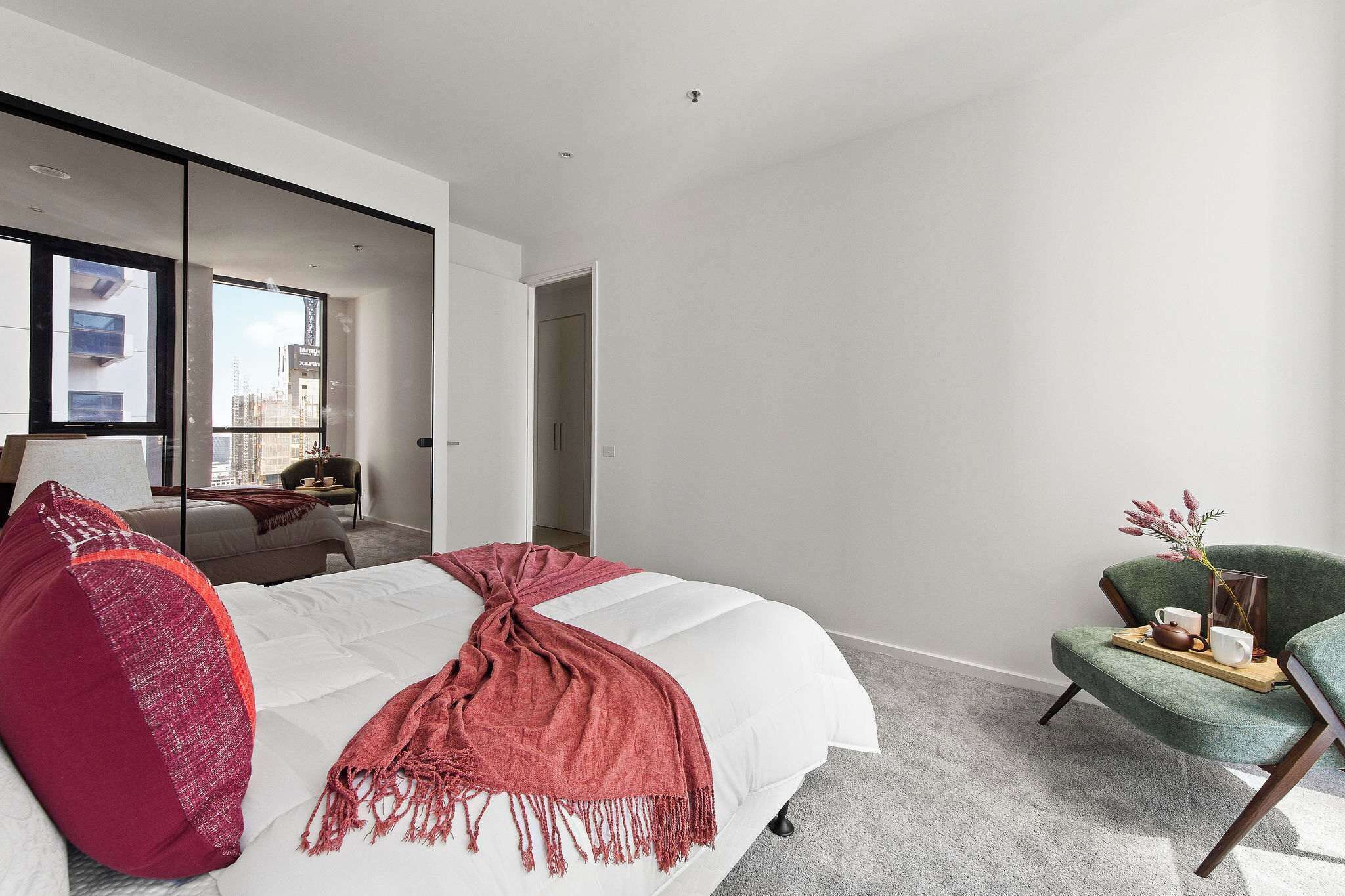 Un dormitorio moderno con una cama grande, un sillón verde y vistas a la ciudad a través de un ventanal.