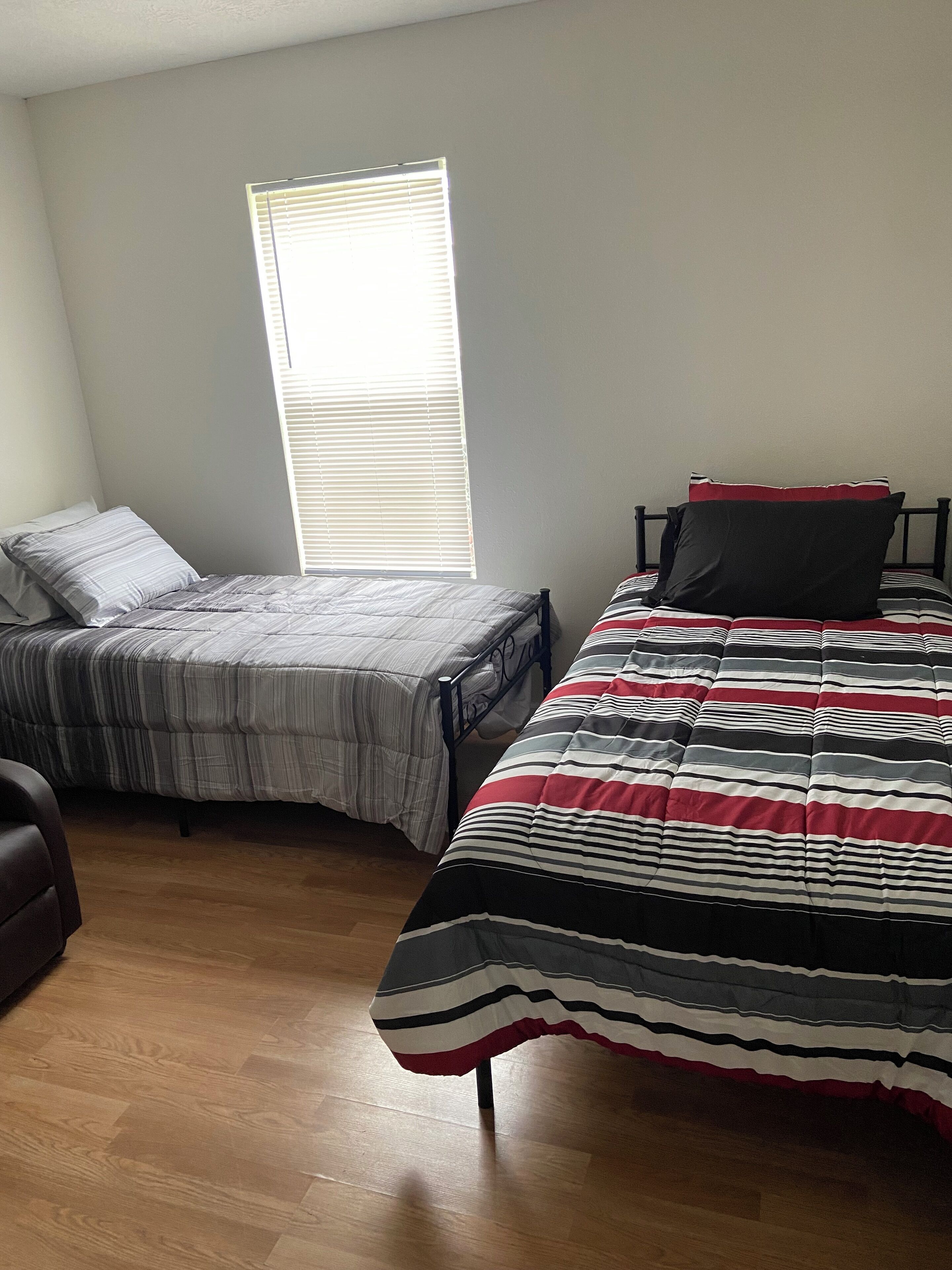 A bedroom with two beds, wooden flooring, and a window with blinds.
