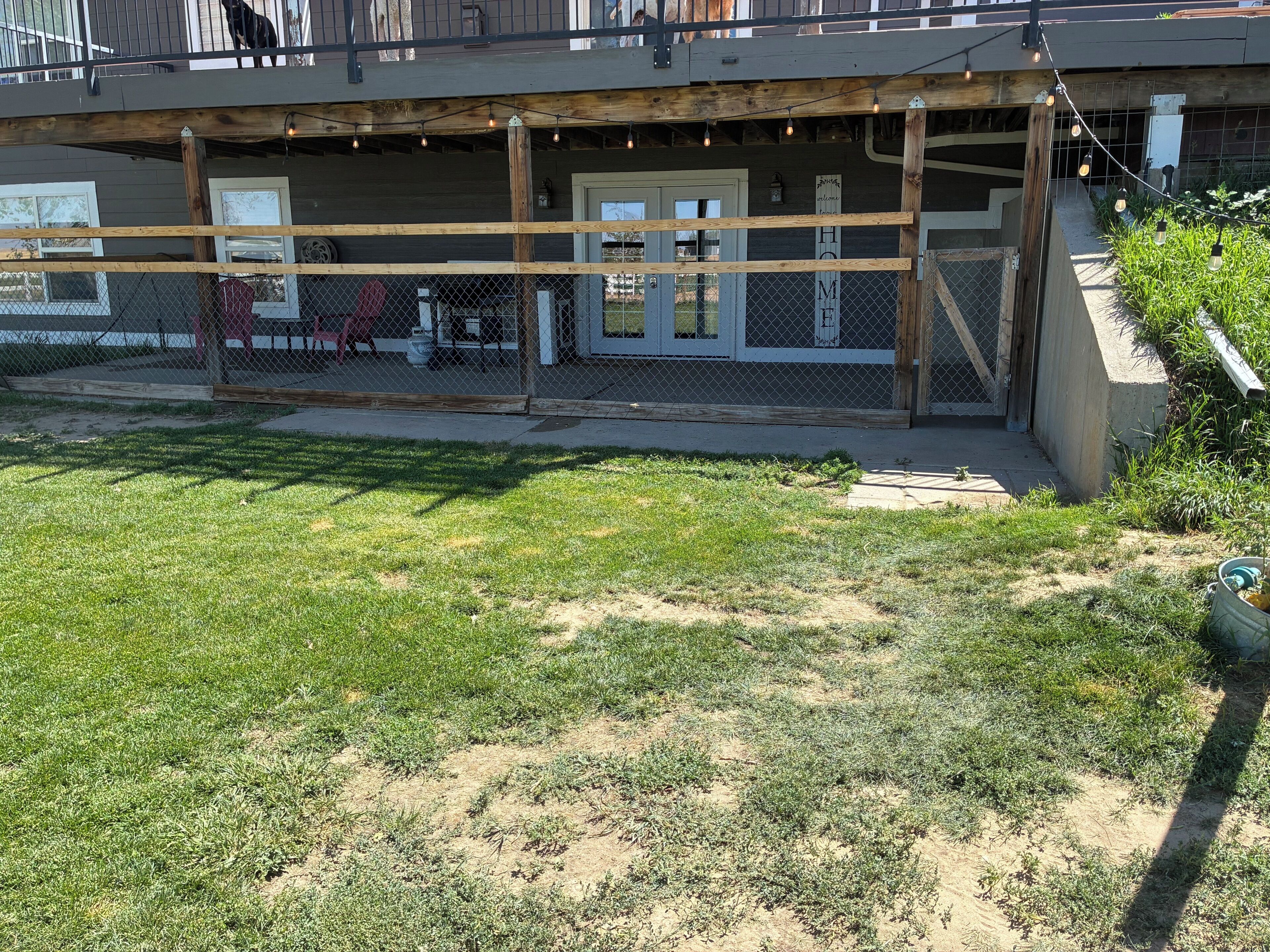 Un espacio al aire libre cercado con terraza de madera, zona de estar cubierta y césped.
