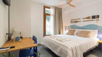 Un dormitorio con cama, escritorio, sillas, ventilador de techo y ventana con cortinas.