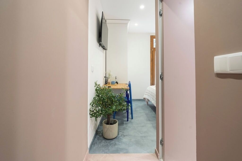 Un pasillo estrecho con una zona de comedor que incluye una mesa, sillas, una planta en maceta y una cama al fondo.
