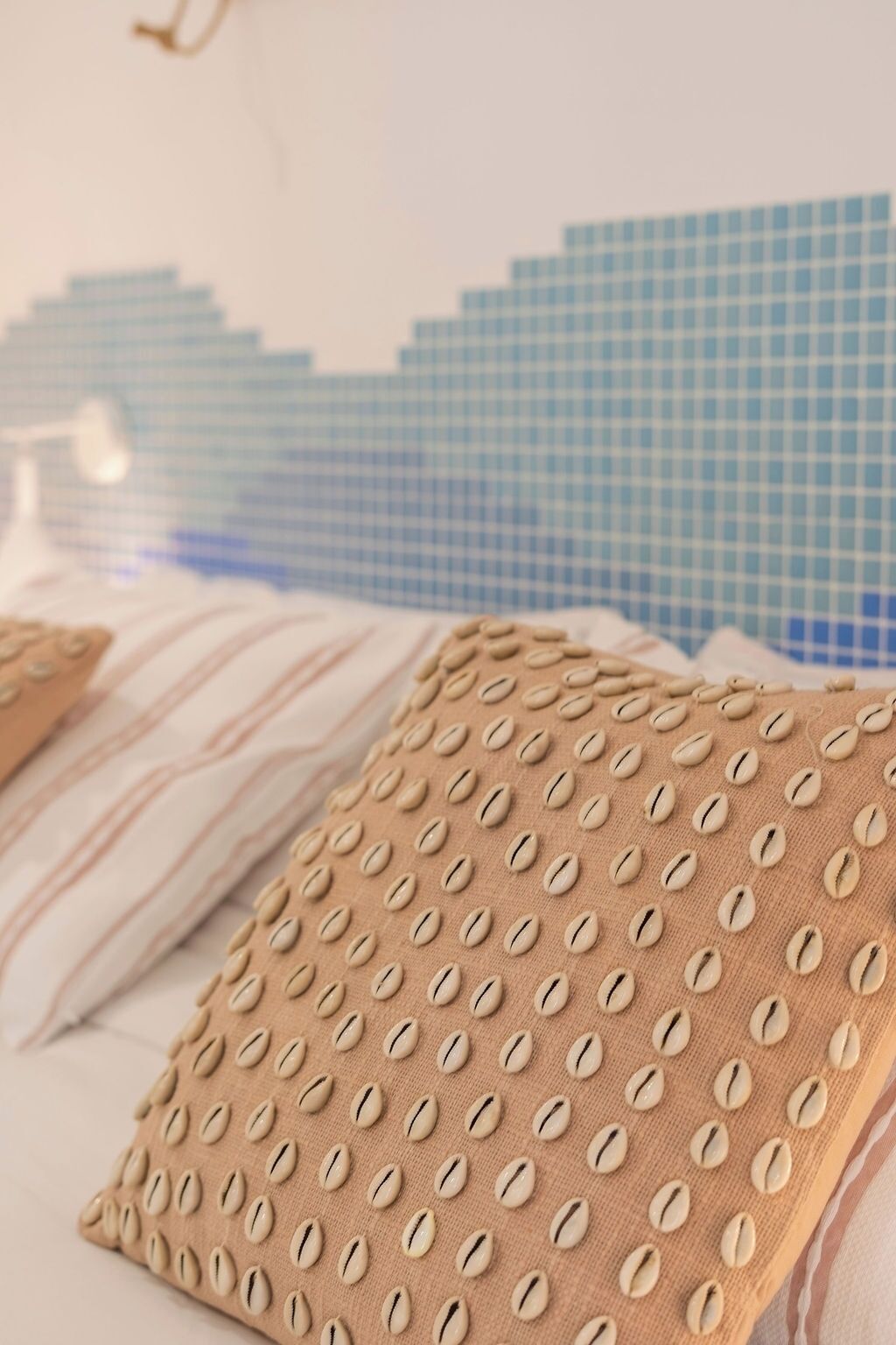 Een bed met een gestructureerd beige kussen en een gestreept kussen, voor een muur met een blauw-wit geruit patroon.