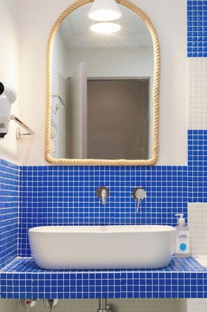 Ein Badezimmer mit weißem Waschbecken, blauen Fliesenwänden, einem spiegelartigen Rahmen aus Seil und einem Handtrockner.