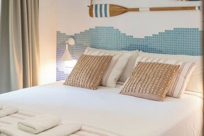 Ein ordentlich bezogenes Bett mit zwei dekorativen Kissen, einem hölzernen Wandbehang und einer blau gefliesten Wand.