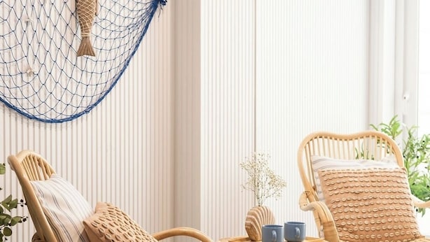 Twee rieten stoelen met kussens, een klein tafeltje met twee blauwe mokken, en een decoratieve vis die aan een net aan de muur hangt.