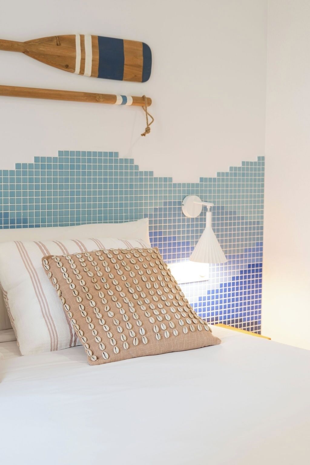 Una cama con un almohadón a rayas y un almohadón texturizado, una paleta de madera y una pared con mosaicos azules.