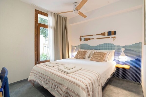 Ein Schlafzimmer mit einem Bett, einem Deckenventilator, einem Fenster mit Vorhängen und einem Wandregal mit einer Lampe.