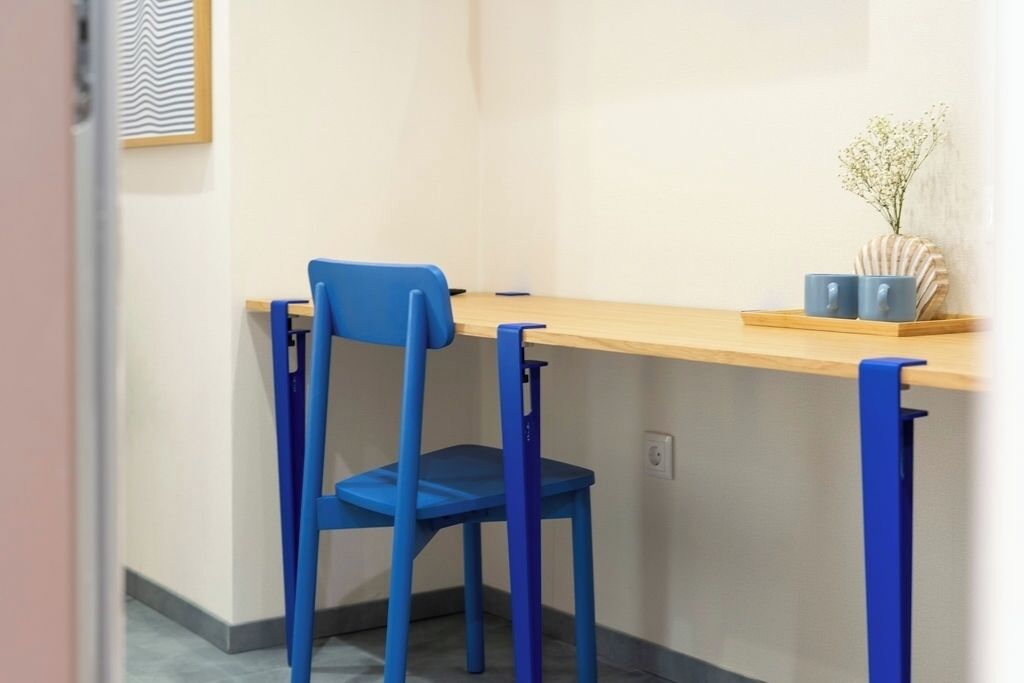 A blue chair and table in a room with a light-colored wall and a framed picture.