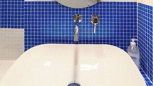 Een badkamer met een wit wastafel, blauwe betegelde wanden, een spiegel en een deur.