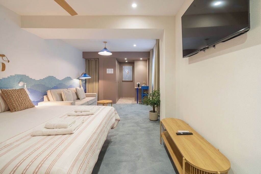 Una habitación de hotel con cama, escritorio, televisor y una planta en maceta.