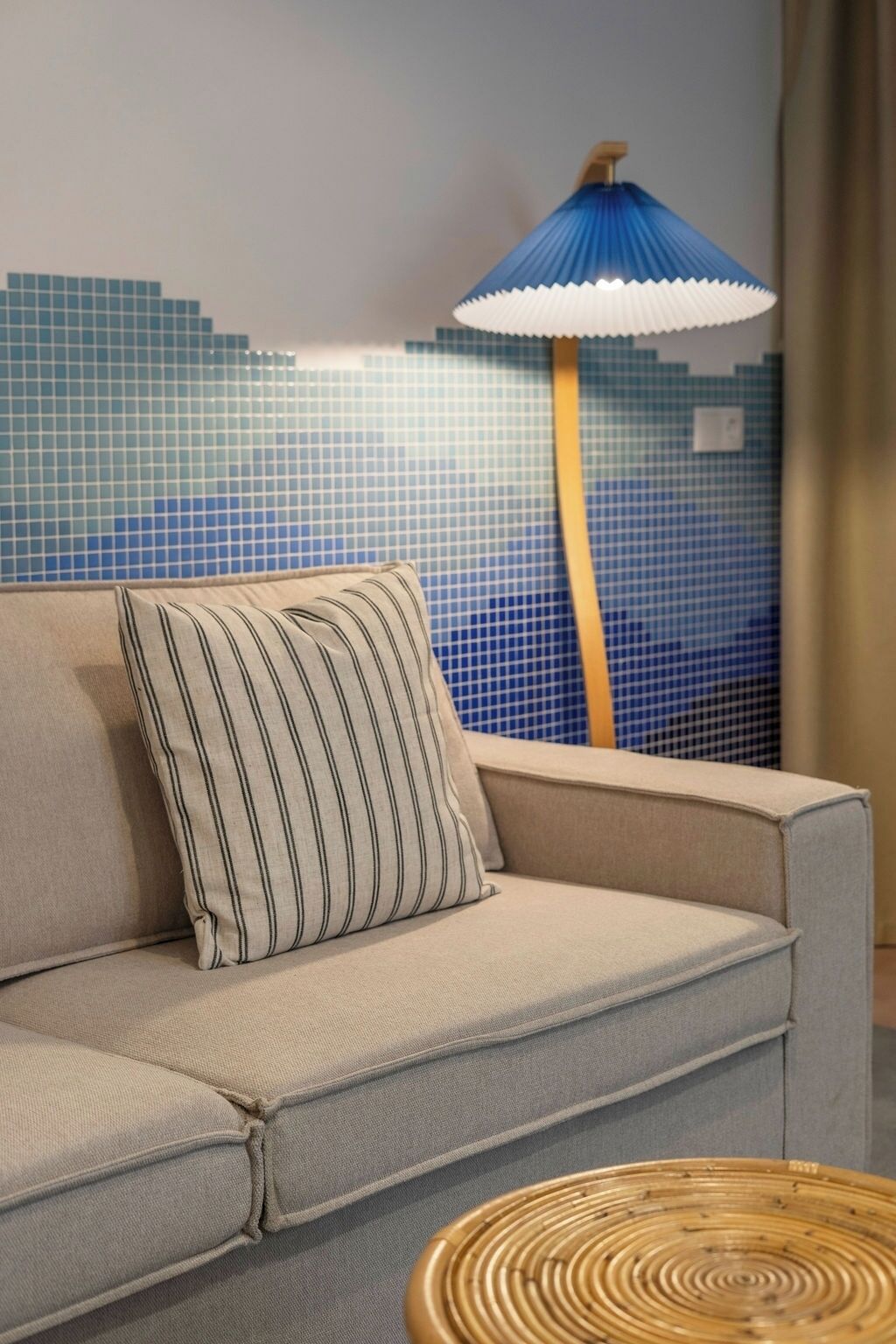 A sofa with a striped pillow, a blue and white lamp, and a tiled wall.