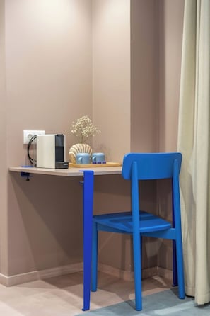 Escritorio en esquina con una silla azul, un jarrón pequeño con flores y una regleta.
