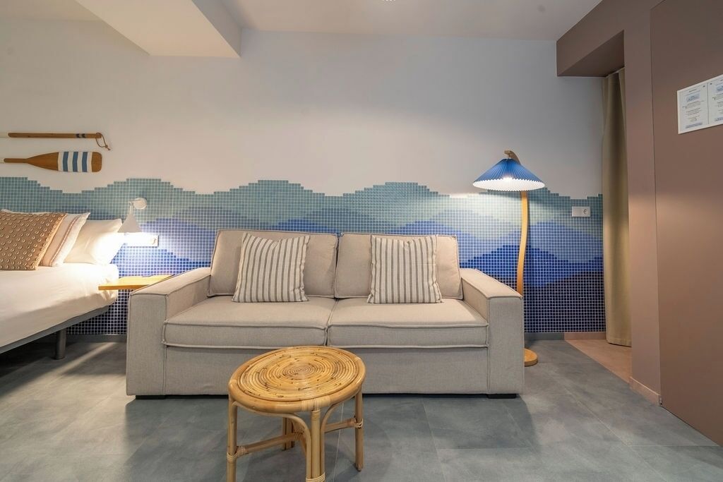 Una habitación de hotel moderna con sofá, una pequeña mesa redonda, una lámpara y una pared con diseño de mosaico azul.